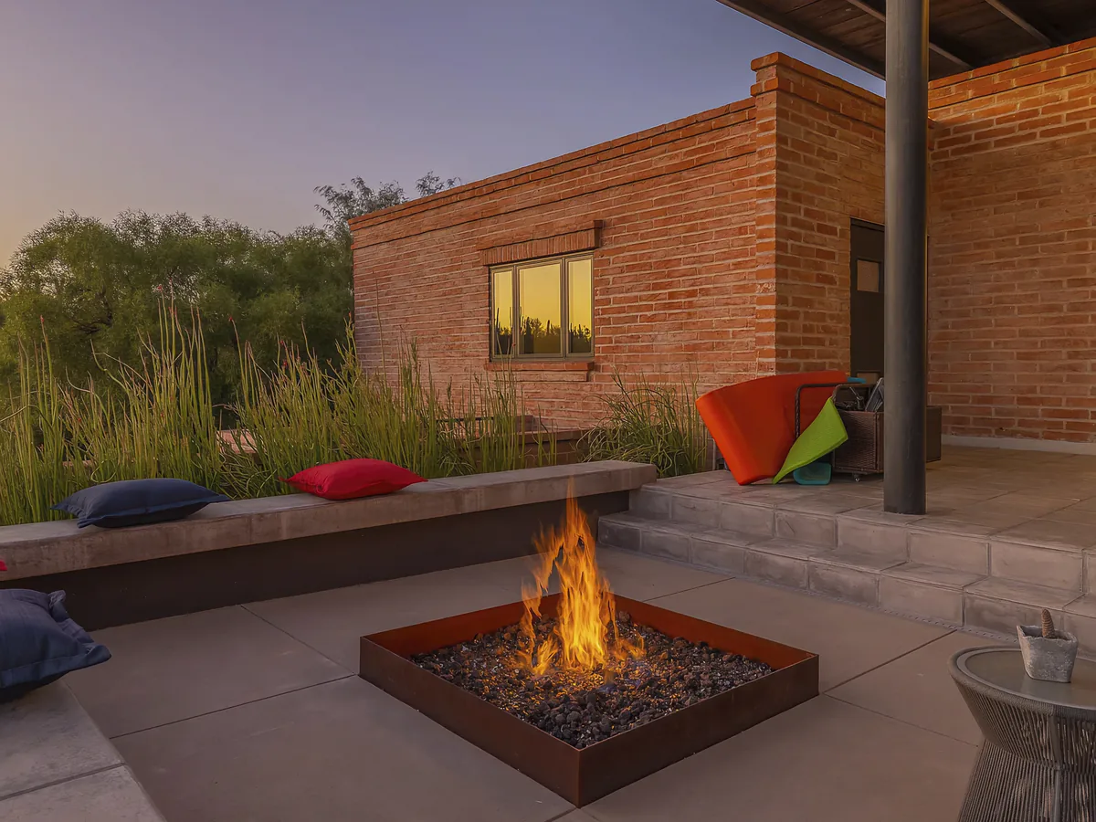 Steel fire pit and bench seat against a burnt adobe wall at dusk, Camino Antonio