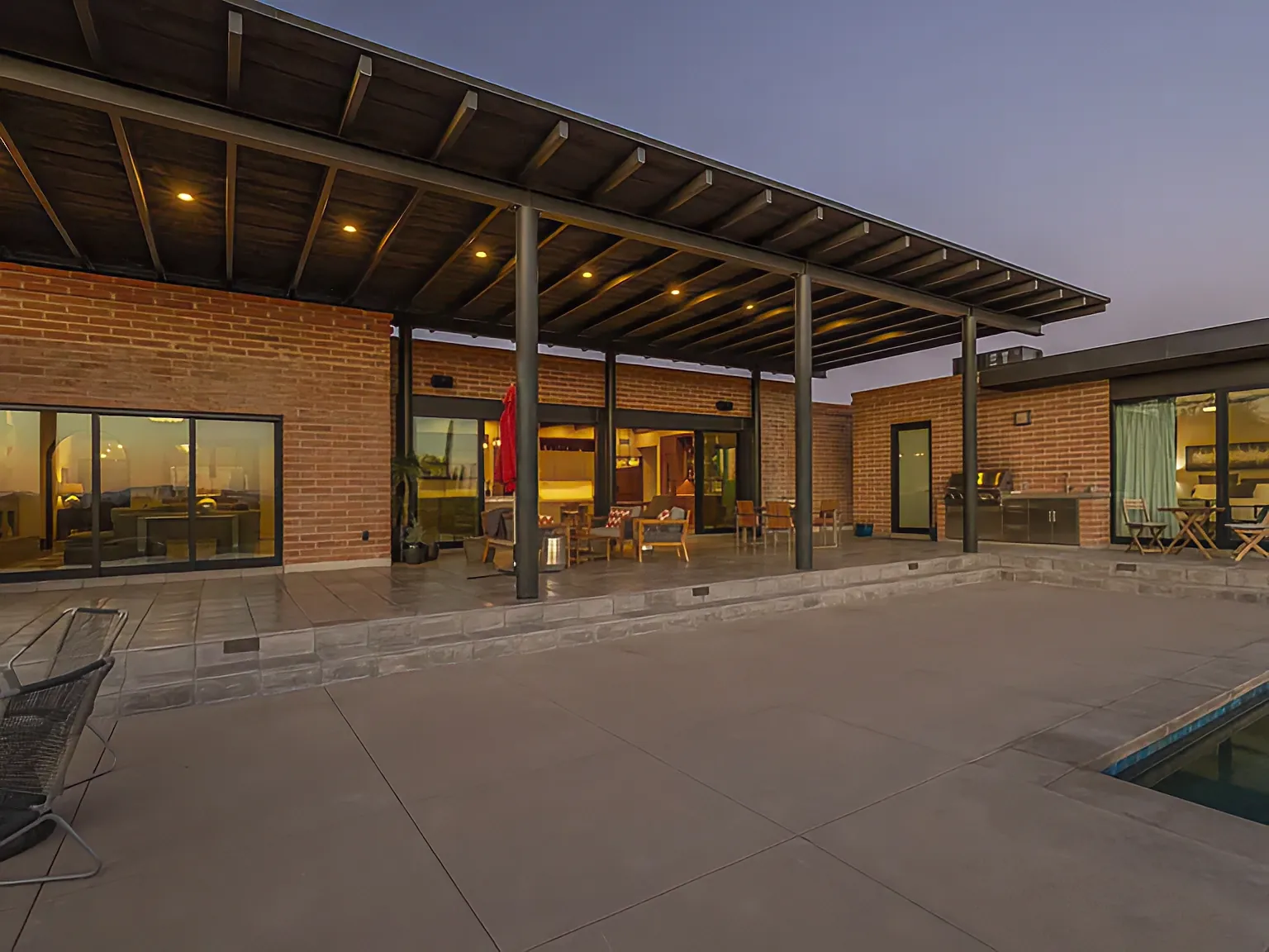 Covered patio and pool at Camino Antonio at dusk, burnt adobe and steel with the interior lit behind