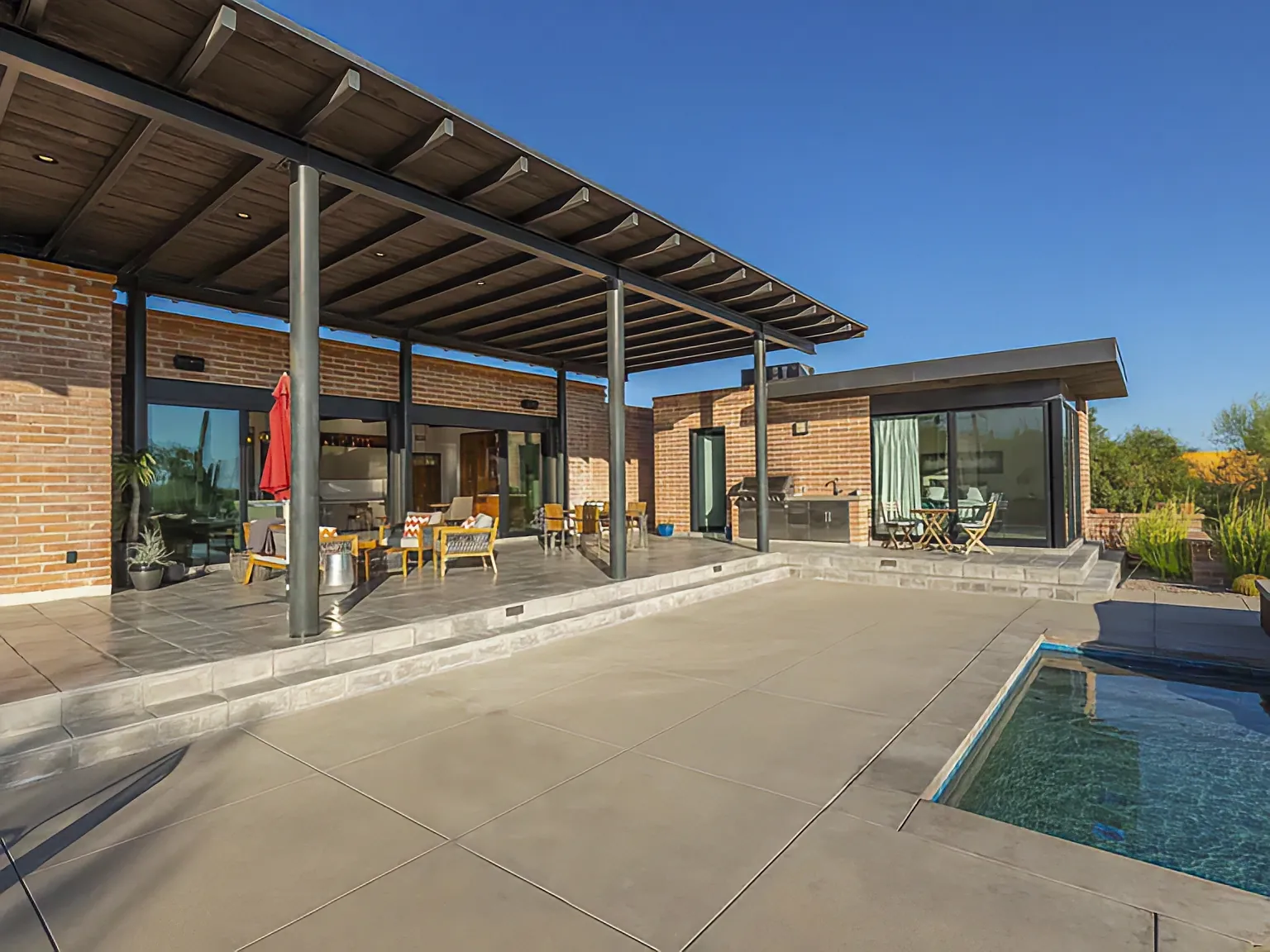 Covered patio and pool at Camino Antonio, steel posts and burnt adobe in afternoon light