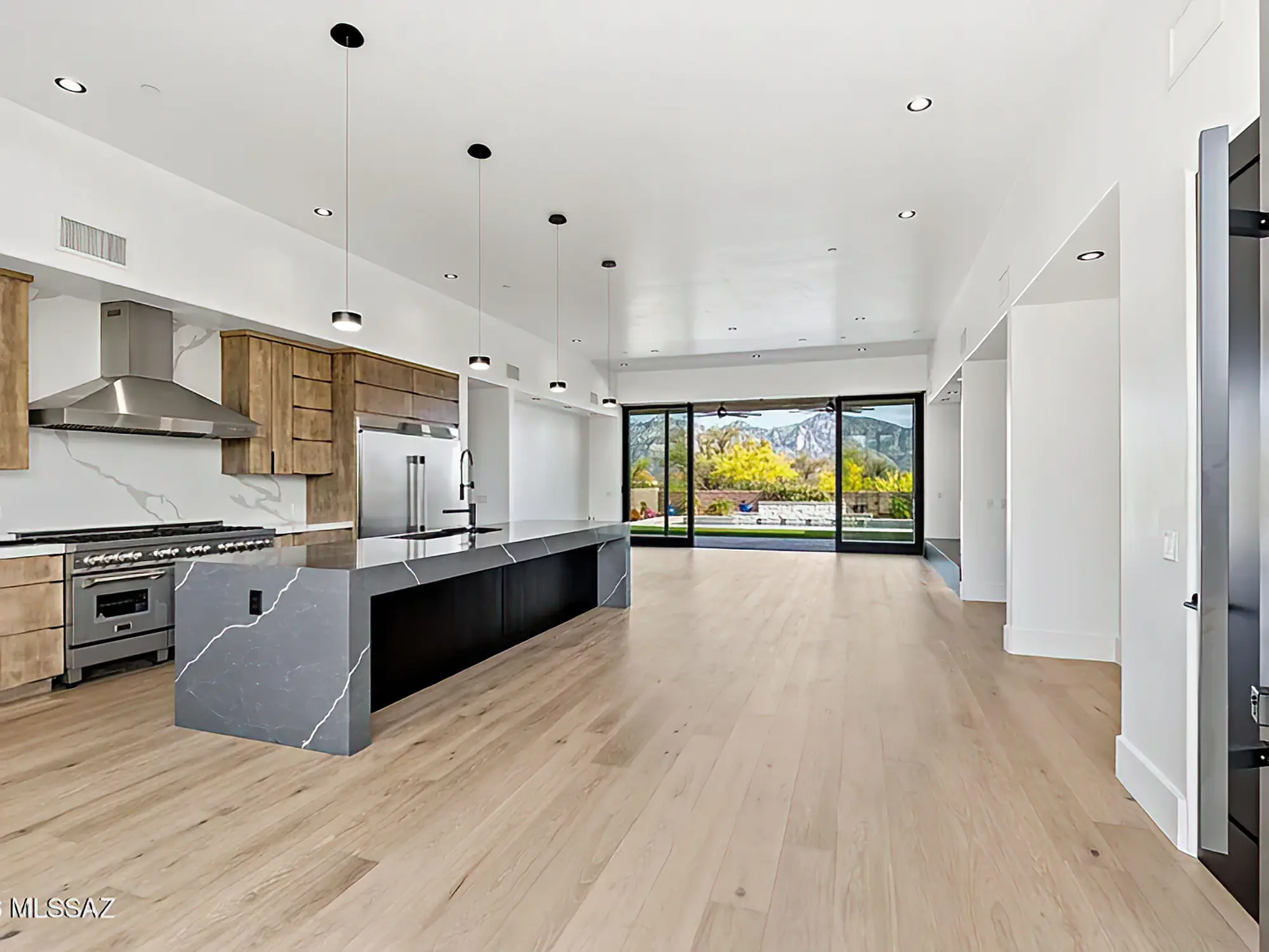 Open kitchen and great room at The Estates at Honey Bee Ridge, waterfall-edge island with the Catalina Mountains through glass doors beyond